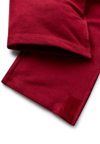 Detailní záběr na složené červené textilní rukávy s přišitými lemy a štítkem "DREAM" na jednom rukávu.