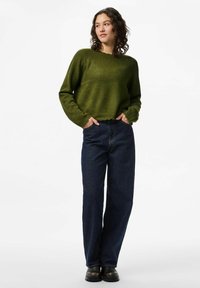 Donkergroen, kort trui met een losse pasvorm en geribbelde zoom, gecombineerd met hooglopende donkerblauwe jeans en zwarte enkellaarsjes.