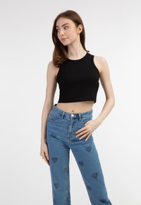 Fekete bordázott crop top, amelyet magas derekú, szív alakú mintázatú kék farmernadrággal párosítottak. A modell egy semleges háttér előtt áll.