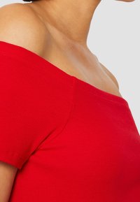 Rød ribbet off-the-shoulder top med korte ærmer og tætsiddende design, der fremhæver blød tekstur og en glat halsudskæring.