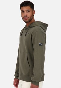 Olijfgroene hoodie met een trekkoordcapuchon, voorzak en geribde manchetten. Bevat een logopatch op de mouw en heeft een gladde stoftextuur.