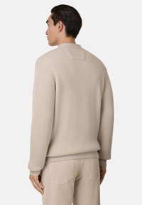 Beżowy sweter prążkowany z okrągłym dekoltem i opadającymi ramionami, z teksturowanej tkaniny i luźnym krojem, zestawiony z jasnobeżowymi spodniami.