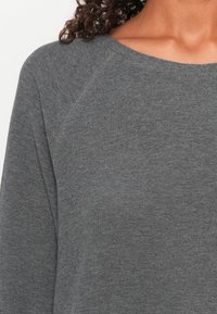 Grå, teksturert genser med vid hals og raglanermer, laget av mykt strikket stoff og med et rent, minimalistisk design.