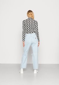 Camisola de manga longa em preto e branco com padrões de formas variadas, combinada com jeans de pernas largas em azul claro, com desgastes visíveis, e sapatilhas brancas.