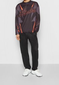 Långärmad svart sporttröja med röda accenter och mesh-textur, tillsammans med svarta trånga byxor och vita sneakers.