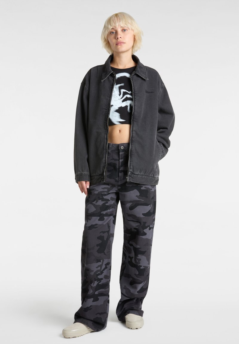 Oversized black denim jacket over a black crop top with a graphic design, paired with loose-fitting camouflage pants in dark tones.