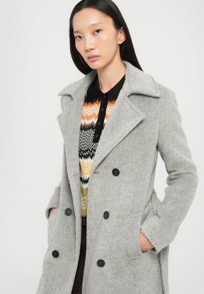 Palton gri din lână cu un rever ascuțit, design dublu-butoan și două buzunare frontale. Purtați-l peste un pulover cu un model colorat.