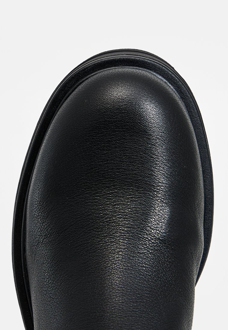 Stivale in pelle nera con una punta arrotondata, una texture liscia e una lieve lucentezza, con un dettaglio di cucitura lungo la parte superiore.