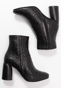 Botas de tobillo negras con textura tejida, puntera afilada y un tacón de bloque resistente. Cierre de cremallera lateral para una fácil puesta.
