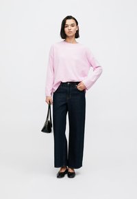 Ανοιχτό ροζ μακρυμάνικη μπλούζα, σκούρο τζιν με φαρδιά μπάτζια, μαύρες μπαλαρίνες και μικρή μαύρη τσάντα χειρός. Το σύνολο χαρακτηρίζεται από απλές γραμμές και άνετη εφαρμογή.