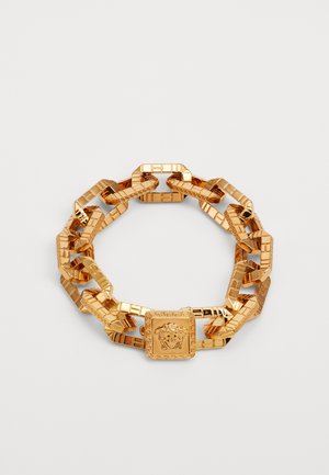 Gold chain bracelet featuring interlocking geometric links, a square central accent with a lion motif, and a shiny, polished finish.