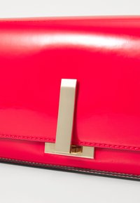 Rosa lakkert lær clutch med en metallisk gulllås og minimalistisk design. Har en glatt tekstur og kontrasterende svart stikking.