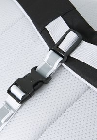 Fivela preta em um tecido de malha branca. O design apresenta uma superfície texturizada com um destaque preto contrastante e uma correia de ajuste cinza.