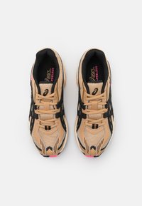 Pár béžových a černých tenisek ASICS Preleus s růžovými akcenty, viděný zeshora na čistém bílém pozadí.