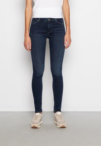 Jeans skinny blu scuro con una texture in denim liscia e leggermente elasticizzata. Design a cinque tasche e chiusura con bottone classica in vita.