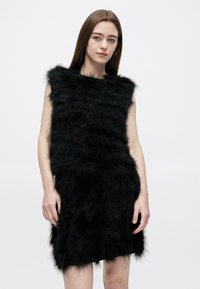 Sort ærmeløs kjole lavet af struktureret imiteret pels med vandrette striber og kort kant. Blødt og tæt udseende.