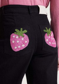 Pantalones negros con fresas bordadas en rosa en cada bolsillo trasero, combinados con una camiseta de manga larga rosa.