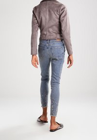 Giacca in pelle grigia, jeans skinny blu con dettagli floreali ricamati all'orlo e sandali neri a ciabatta.