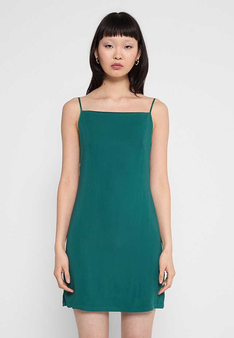 Grünes Slipkleid mit spaghettiartigen Trägern, geradem Ausschnitt und glattem Stoff. Knielanges Design mit seitlichen Schlitzen für mehr Bewegungsfreiheit.