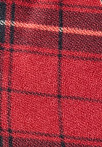 Κόκκινο λουστρινάτο ύφασμα με υφασμένο ανάγλυφο σχέδιο, με μαύρες και κίτρινες γραμμές πλέγματος. Τα τετράγωνα έχουν διαφορετικά μεγέθη, ενισχύοντας το οπτικό βάθος του μοτίβου.