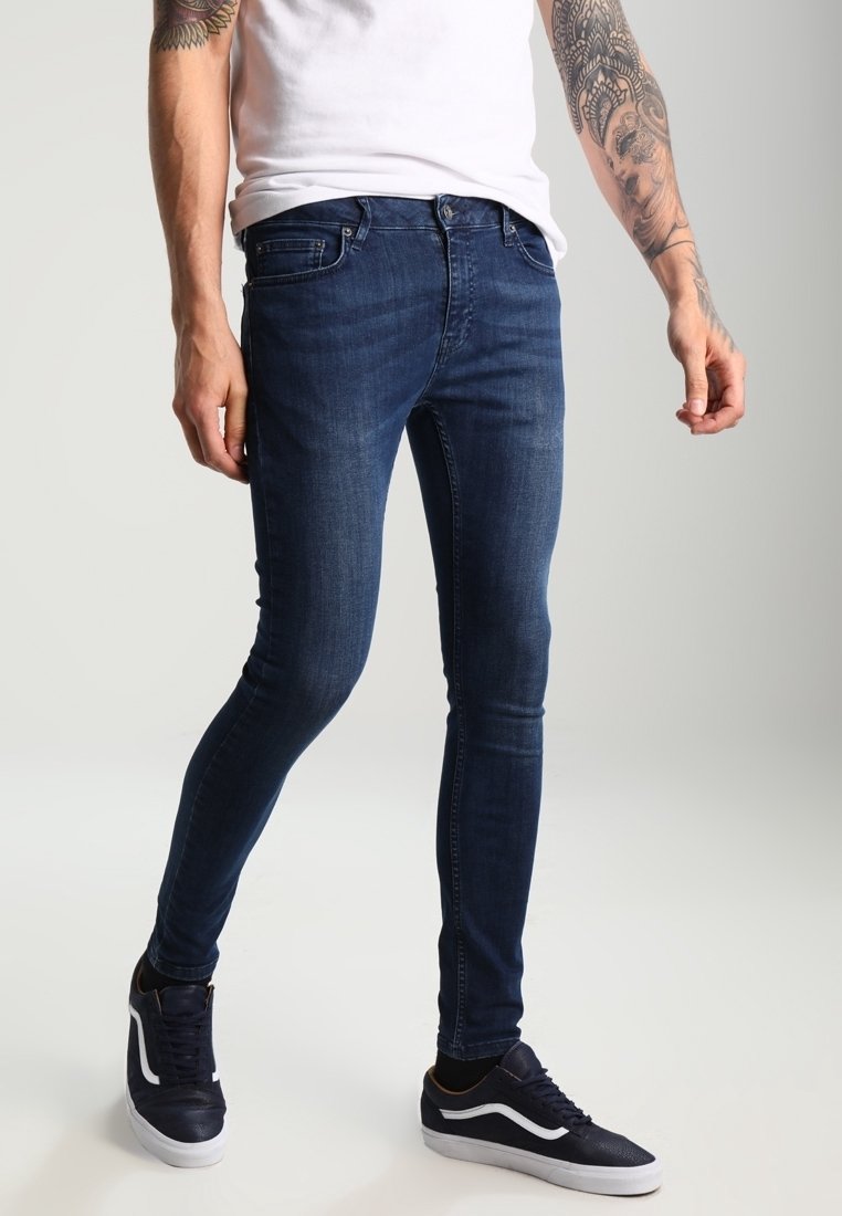 Slim jeans i mörkblå denim med en subtil struktur, utrustade med traditionella fickor och bältesloophål, tillsammans med mörka sneakers.