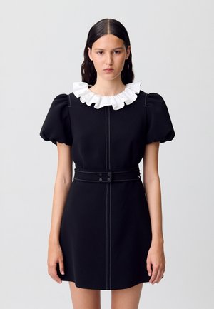 Abito nero con un colletto bianco a volant, maniche a sbuffo e vita aderente. Presenta cuciture a contrasto e una silhouette dritta.
