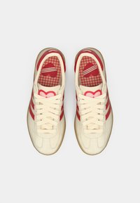 Αθλητικά παπούτσια από κρεμ καμβά με κόκκινες ρίγες και εσωτερική σόλα με σχέδιο καρδιές. Διαθέτουν μπεζ λαστιχένια σόλα και έντονη δέσιμο με κορδόνια.