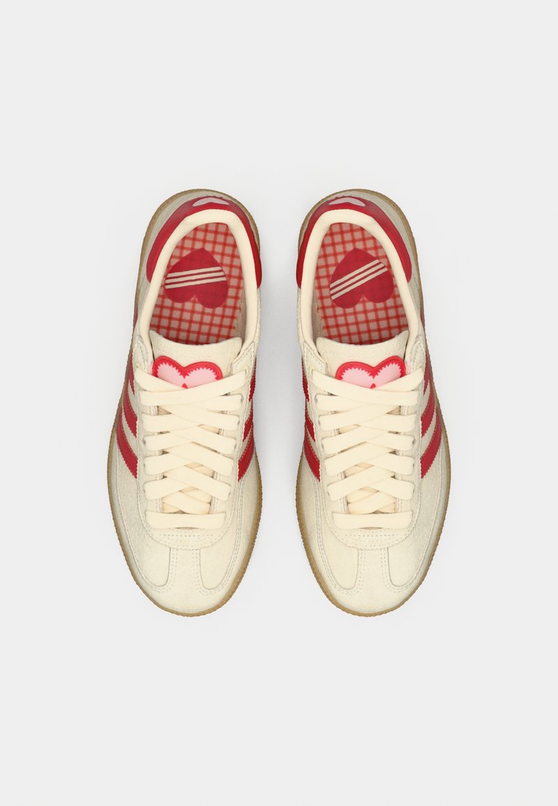 Sneakers in cream canvas with red stripes and heart-patterned insole. Features beige rubber sole and prominent lace-up closure.
