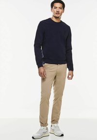 Marinblå crew-neck sweatshirt, beige chinos och vita sneakers. Sweatshirten har en liten logotyp på bröstet och ribbade muddar.