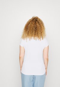 Vit ribbad kortärmad topp, figursydd design, mjuk textur, ihop med ljusblå avslappnade jeans. Bakvy, vågigt hår.