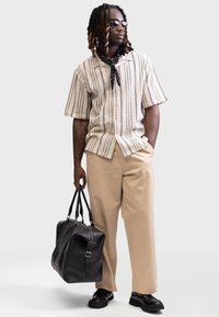 Camisa de manga corta a rayas beige, pantalones beige, bolsa de cuero negro y zapatos negros. Accesorios: bufanda negra y gafas de sol.
