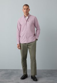 Cămașă roz deschis cu nasturi, cu mâneci lungi, buzunar mic și pantaloni kaki. Mocasini negri cu accente aurii contrastante. Design simplu, cambrat.