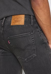 Närbild av svarta Levi's jeans bakficka och lädermärkespatch på en person som bär en mörkgrå skjorta.