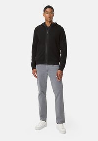 Haut de survêtement zippé noir avec des panneaux texturés, capuche ajustable et poches latérales. Associé à un jean gris clair et des baskets blanches.
