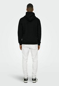 Sort hætte sweatshirt med ribbede manchetter og kant, parret med hvide bukser og sorte sneakers. Struktureret stof, afslappet pasform, bagudsigt.