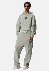 Grijze oversized hoodie met cropped ontwerp, voorzak en zwart logo; gecombineerd met bijpassende losse broek en witte sneakers.