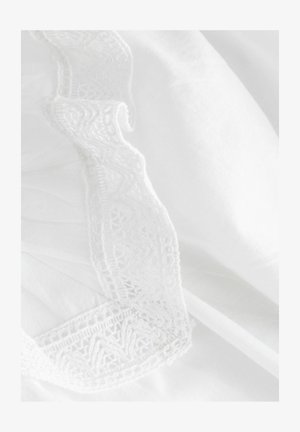 Tissu blanc avec une bordure en dentelle blanche complexe et un bord ondulé, mettant en valeur des détails fins et une texture douce.