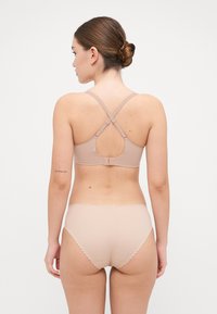 Beige bra and high-waisted briefs made of smooth material. The bra features a crossed back design and adjustable straps with scalloped edges.