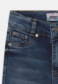Jeans de mezclilla azul oscuro con un diseño de cinco bolsillos, costuras visibles, acentos de metal y una etiqueta que dice "Blue Effect".