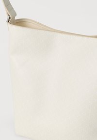 Μπεζ τσάντα ώμου με υφή επιφάνειας που έχει γεωμετρικό μοτίβο και απλό λουρί. Το εσωτερικό της είναι λείο και χωρίς διακοσμητικά.