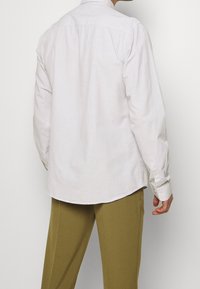 Camicia chiara con bottoni, colletto classico, maniche lunghe e orlo curvo; realizzata in un tessuto strutturato per una vestibilità rilassata.