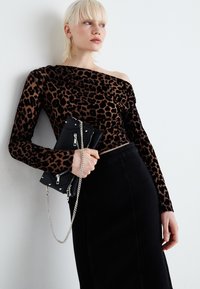 Top z leopardskim vzorcem, z dolgimi rokavi in naramnicami, ki padajo s rame; žametna tekstura. Črna krila z visokim pasom; drži črno torbico s verigo.