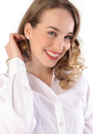Parelstuds op een model met lang, golvend haar, gekleed in een wit overhemd. De oorbellen hebben drie parels in een lijn.