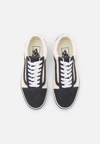 Schwarze und cremefarbene Wildledersneaker mit weißen Schnürsenkeln, die einen kontrastierenden schwarzen Streifen entlang der Seiten und eine weiße Gummisohle aufweisen.