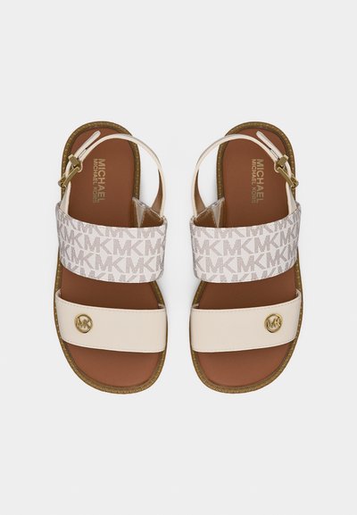 Μπεζ και λευκά σανδάλια Michael Kors με επίπεδη σόλα, λουράκια στον αστράγαλο, φαρδιά λουριά με μονόγραμμα και χρυσές λεπτομέρειες λογότυπου στα λουριά των δακτύλων.