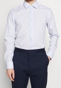 Lichtblauw overhemd met spreadkraag, gemaakt van gladde stof, met lange mouwen en een klassieke pasvorm. Draagt bij donkerblauwe broeken.