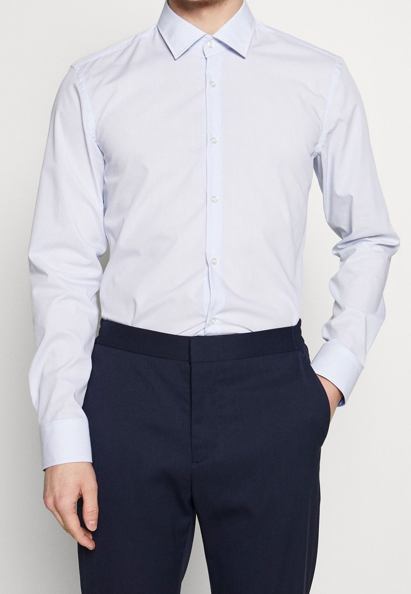 Lichtblauw overhemd met spreadkraag, gemaakt van gladde stof, met lange mouwen en een klassieke pasvorm. Draagt bij donkerblauwe broeken.