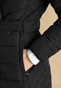 Käsi on musta tikkjakki, millel on elastne vöö, ning valge varrukas on nähtav, varrukal on tikitud "Joules".