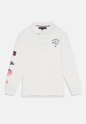 Hvit langermet polo skjorte med krage, med marineblå og røde broderte detaljer og lapper på ermene. Bomullstoff, avslappet passform.