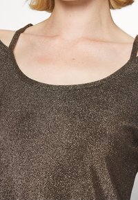 Braunes metallisches Strickoberteil mit Rundhalsausschnitt und schmalen Trägern. Der Stoff hat eine schimmernde Textur mit glitzernden Akzenten.